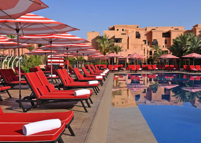Piscina con lettini, ombrelloni e resort sullo sfondo